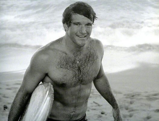 Fred Hemmings with his surfboard on the beach in the 1960s